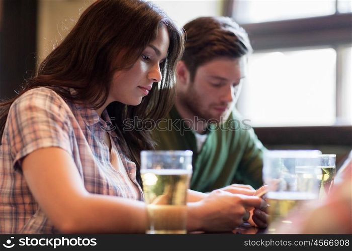 people, leisure, technology and communication concept - group of friends with smartphones drinking beer and at bar or pub