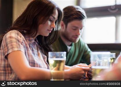 people, leisure, technology and communication concept - group of friends with smartphones drinking beer and at bar or pub