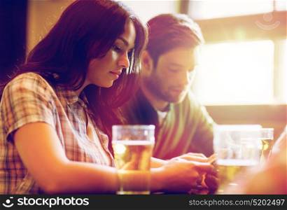 people, leisure, technology and communication concept - group of friends with smartphones drinking beer and at bar or pub. friends with smartphones drinking beer and at pub