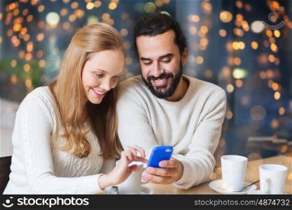 people, leisure, technology and dating concept - happy couple with smartphone drinking tea or coffee at cafe over holidays lights background