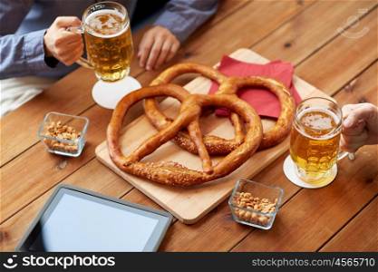 people, leisure, technology and drinks concept - close up of male friends drinking beer with pretzels, peanuts and tablet pc computer on table at bar or pub