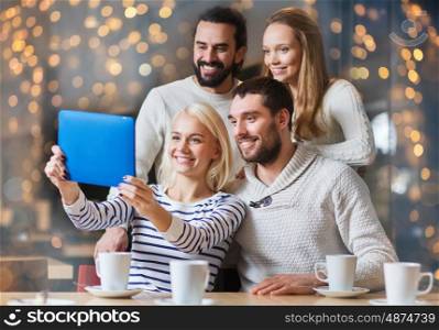 people, leisure, technology and friendship concept - happy friends with tablet pc computer taking selfie at cafe over holidays lights background