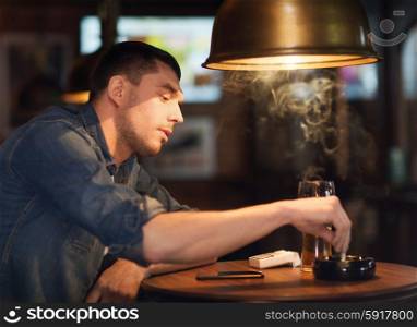 people, lifestyle and bad habits concept - man drinking beer and smoking and extinguishing his cigarette at bar or pub