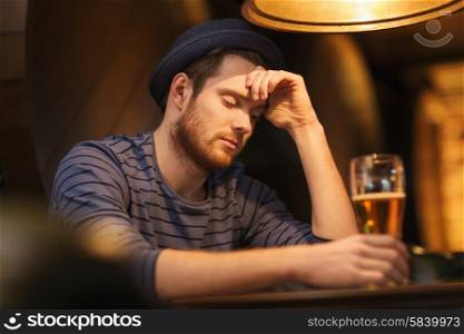 people, loneliness, alcohol and lifestyle concept - unhappy single young man in hat drinking beer at bar or pub