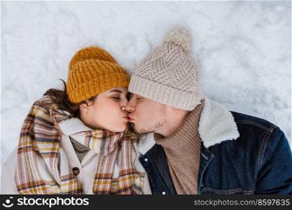 people, love and leisure concept - happy couple kissing lying on snow in winter. happy couple kissing lying on snow in winter