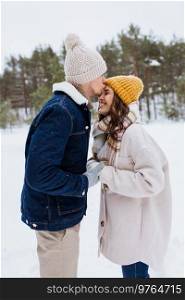 people, love and leisure concept - happy man kissing woman to forehead in winter forest. happy man kissing woman to forehead in winter