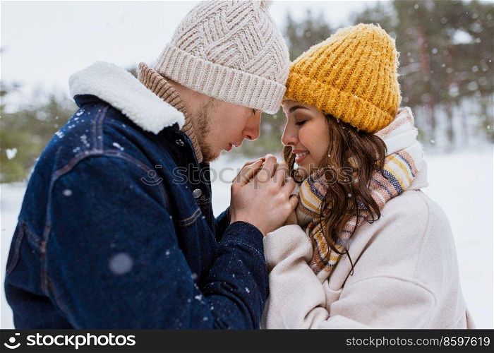 people, love and leisure concept - happy man warming woman’s hands in winter park. happy man warming woman’s hands in winter park