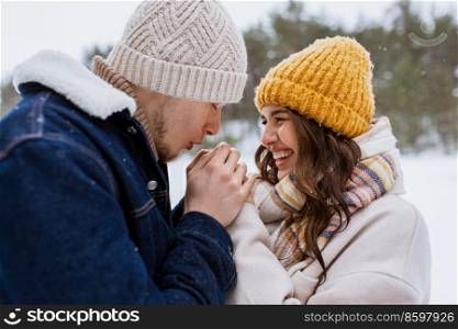 people, love and leisure concept - happy man warming woman’s hands in winter park. happy man warming woman’s hands in winter park