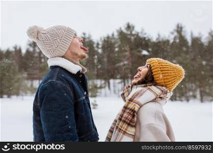people, love and leisure concept - happy smiling couple catching snow with open mouth in winter. happy smiling couple catching snow in winter