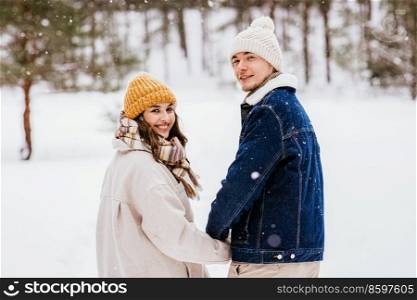 people, love and leisure concept - happy smiling couple walking and looking back in winter forest. happy smiling couple walking in winter forest