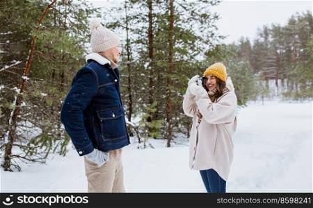 people, love and leisure concept - happy smiling woman photographing man in winter forest. happy woman photographing man in winter forest