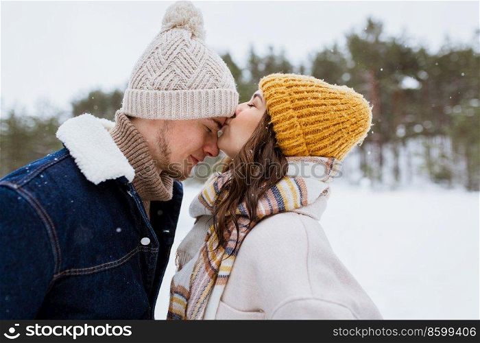 people, love and leisure concept - happy woman kissing man to forehead in winter forest. happy woman kissing man to forehead in winter