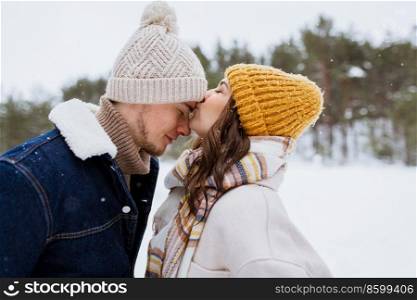 people, love and leisure concept - happy woman kissing man to forehead in winter forest. happy woman kissing man to forehead in winter