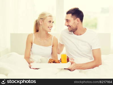 people, love, care and happiness concept - happy couple having breakfast in bed at home