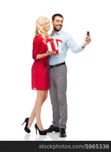 people, love, couple, technology and holidays concept - happy young woman and man with birthday presents taking selfie by smartphone