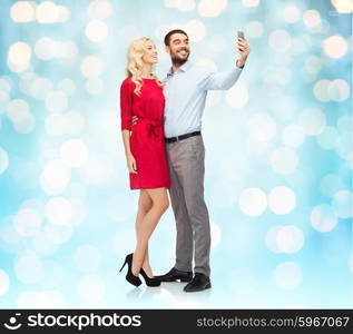 people, love, couple, technology and holidays concept - happy young woman and man taking selfie with smartphone and hugging over blue lights background