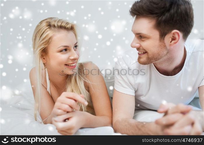people, love, relationships, christmas and winter holidays concept - happy couple lying in bed at home over snow