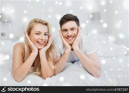 people, love, relationships, christmas and winter holidays concept - happy couple lying in bed at home over snow