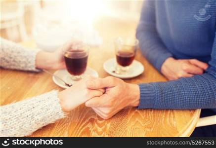 people, love, romance and dating concept - close up of happy couple drinking tea and holding hands at cafe or restaurant. close up of couple holding hands at restaurant