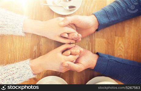 people, love, romance and dating concept - close up of happy couple drinking tea and holding hands at cafe or restaurant. close up of couple holding hands at restaurant