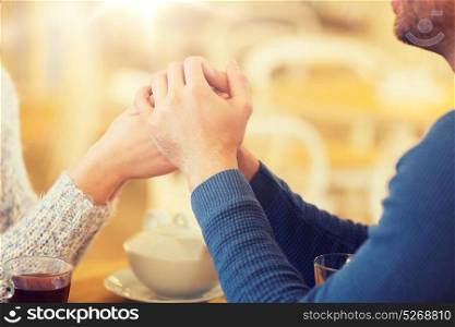 people, love, romance and dating concept - close up of happy couple drinking tea and holding hands at cafe or restaurant. happy couple with tea holding hands at restaurant
