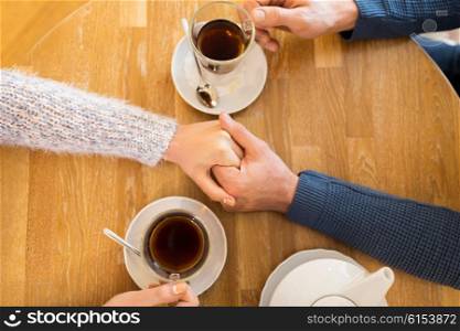 people, love, romance and dating concept - close up of happy couple drinking tea and holding hands at cafe or restaurant