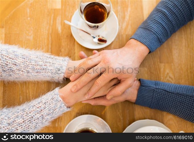 people, love, romance and dating concept - close up of happy couple drinking tea and holding hands at cafe or restaurant