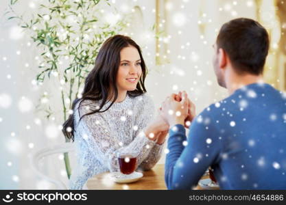 people, love, romance and dating concept - happy couple drinking tea and holding hands at cafe or restaurant