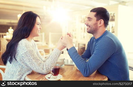 people, love, romance and dating concept - happy couple drinking tea and holding hands at cafe or restaurant. happy couple with tea holding hands at restaurant