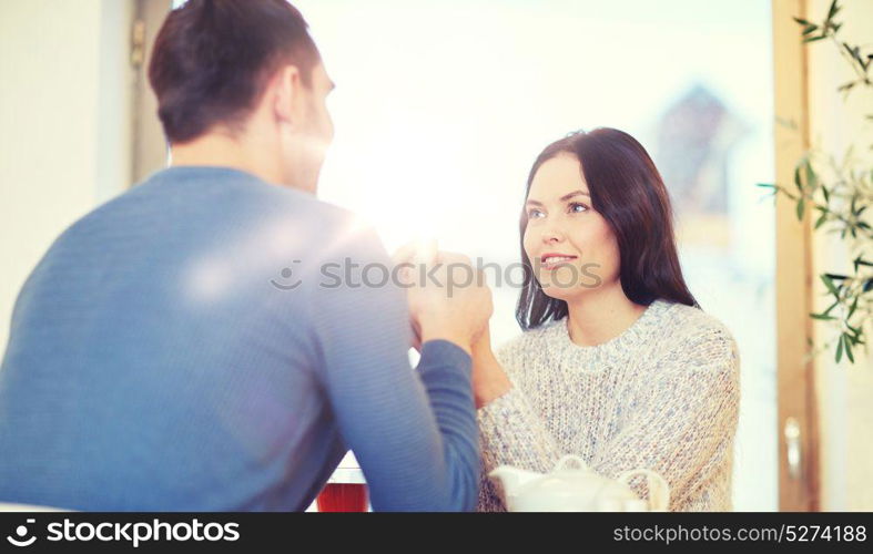 people, love, romance and dating concept - happy couple drinking tea and holding hands at cafe or restaurant. happy couple with tea holding hands at restaurant