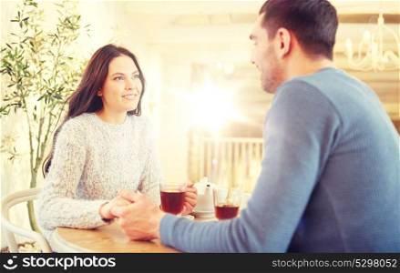 people, love, romance and dating concept - happy couple drinking tea and holding hands at cafe or restaurant. happy couple with tea holding hands at restaurant