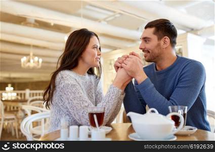 people, love, romance and dating concept - happy couple drinking tea and holding hands at cafe or restaurant