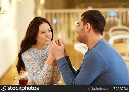 people, love, romance and dating concept - happy couple drinking tea and holding hands at cafe or restaurant