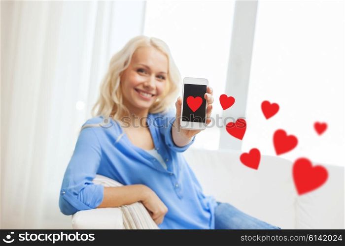 people, love, technology and communication concept - smiling woman showing smartphone with red hearts and sitting on couch at home