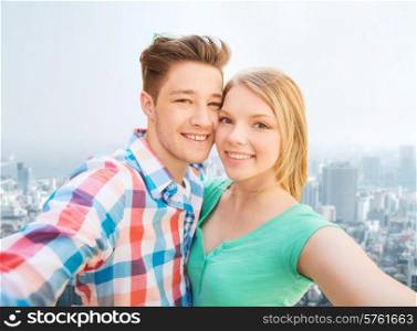 people, love, vacation, technology and summer concept - happy couple taking selfie with smartphone or camera over city background