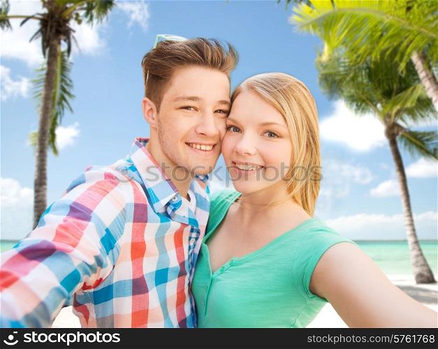 people, love, vacation, technology and summer concept - happy couple taking selfie with smartphone or camera over tropical beach background