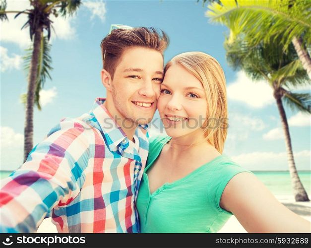 people, love, vacation, technology and summer concept - happy couple taking selfie with smartphone or camera over tropical beach background