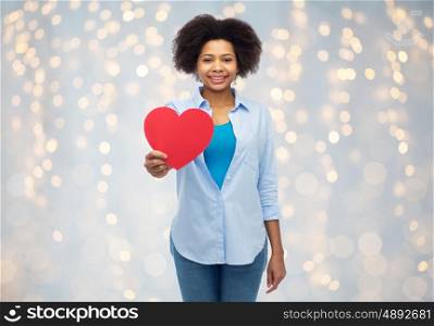 people, love, valentines day and health concept - happy african american young woman with red heart shape over holidays lights background
