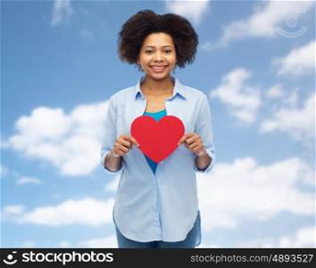 people, love, valentines day and health concept - happy african american young woman with red heart shape over blue sky and clouds background