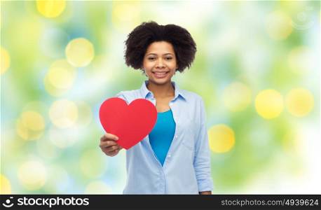 people, love, valentines day and health concept - happy african american young woman with red heart shape over summer green lights background. happy african american woman with red heart shape