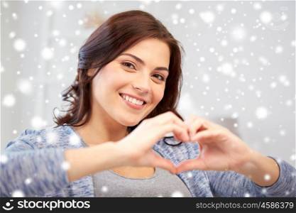 people, love, valentines day, charity and christmas concept - happy young woman showing heart with hands at home over snow