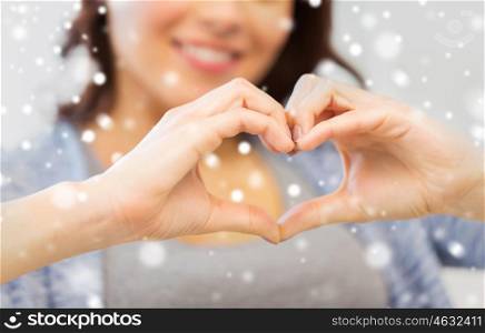 people, love, valentines day, christmas and charity concept - close up of happy young woman showing heart with hands over snow