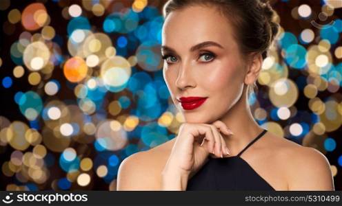 people, luxury and beauty concept - close up of beautiful woman in black with red lips over holidays lights background. beautiful woman in black over lights background