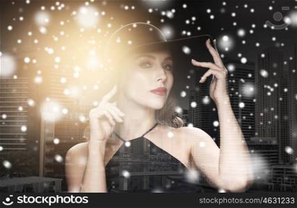 people, luxury and christmas concept - beautiful woman in black hat over dark over dubai city background double exposure with highlight and snow