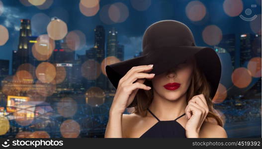 people, luxury and fashion concept - beautiful woman in black hat over night singapore city and lights background