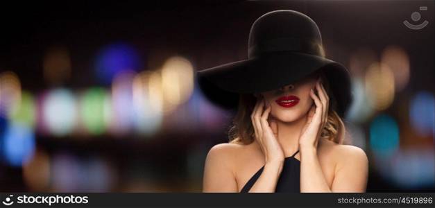 people, luxury and fashion concept - beautiful woman in black hat over blurred night lights background