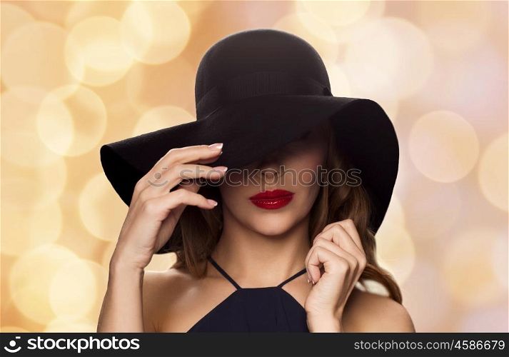 people, luxury and fashion concept - beautiful woman in black hat over holidays lights background