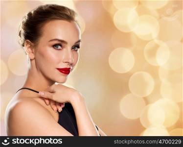 people, luxury and fashion concept - beautiful woman in black with red lips over holidays lights background