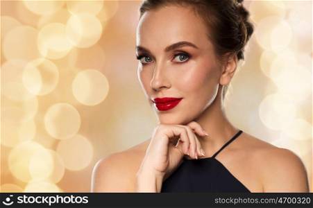 people, luxury and fashion concept - beautiful woman in black with red lips over holidays lights background
