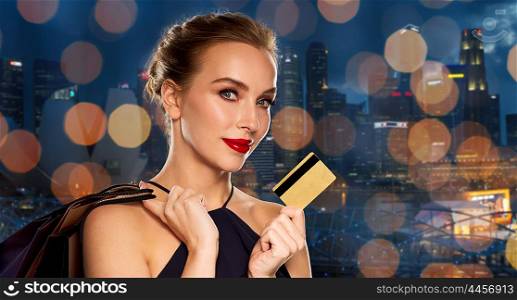 people, luxury and sale concept - beautiful woman with credit card and shopping bags over night singapore city and lights background